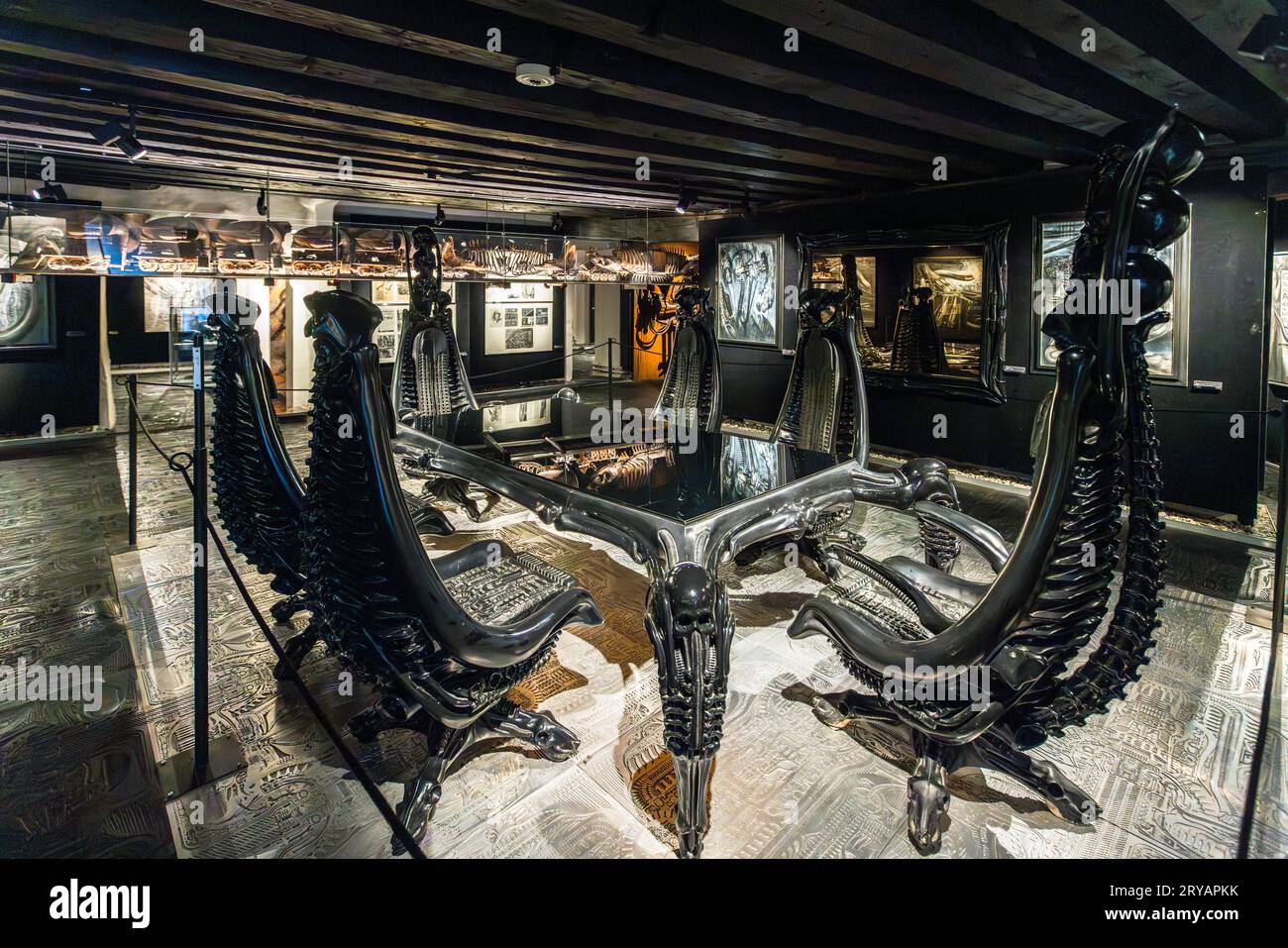 Sedie Harkonnen nere e scheletriche (Sedia Capo Hakoonen) circondano un tavolo corrispondente al Museo HR Giger a Gruyères, nel cantone di Friburgo, Svizzera. Giger ha progettato la serie di mobili, realizzata in alluminio o fibra di vetro nera, per un adattamento cinematografico non prodotto del romanzo di fantascienza "Dune" di Frank Herbert degli anni '70, che doveva essere diretto da Alejandro Jodorowsky. Il barone Harkonnen è il cattivo del romanzo. Il museo è ospitato dal 1998 nello Château St. Germain, che Giger acquistò nel 1997. Foto Stock