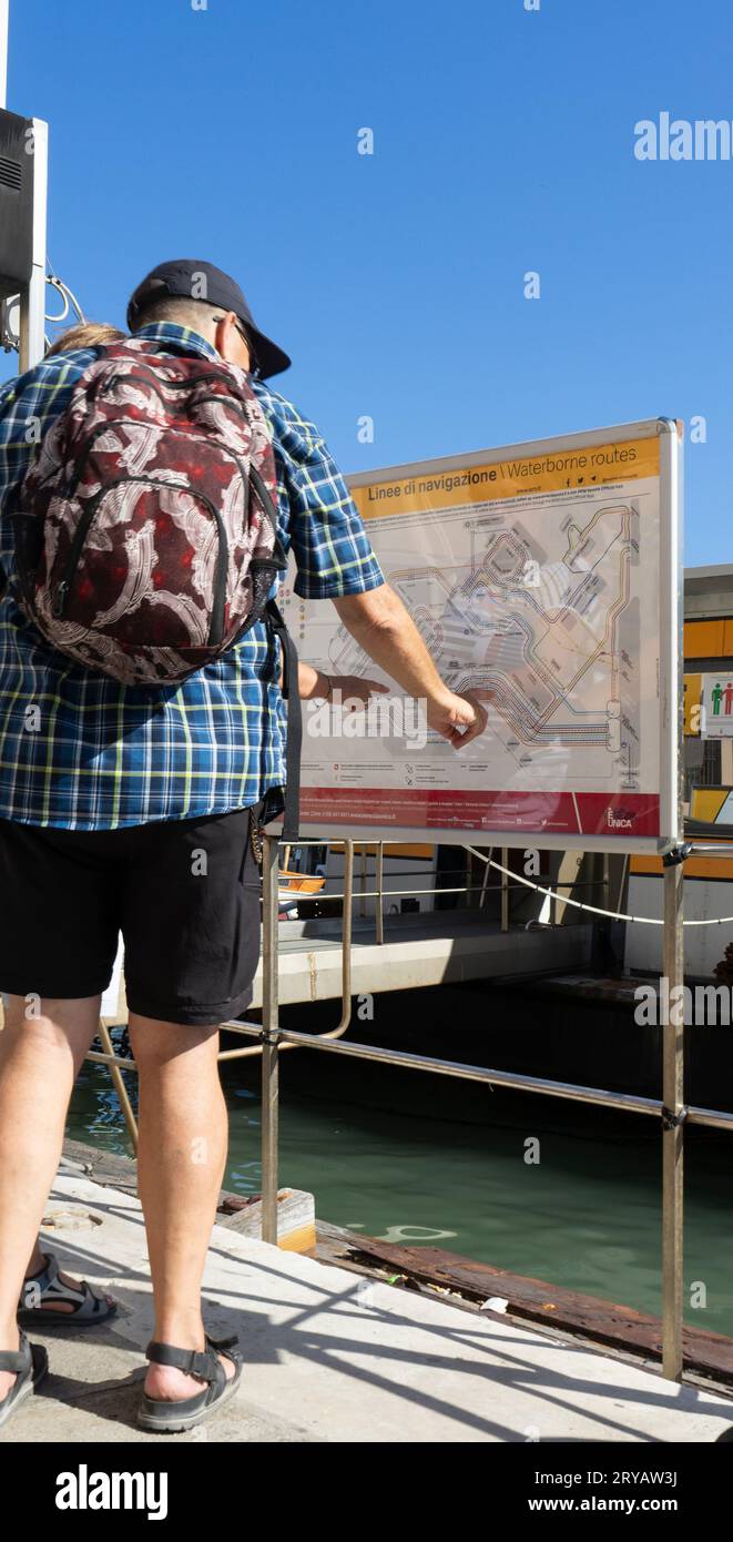 Un turista con zaino in spalla guarda la mappa dei trasporti acquatici della città di Venezia in una giornata di sole. Foto verticale Venezia Italia Foto Stock