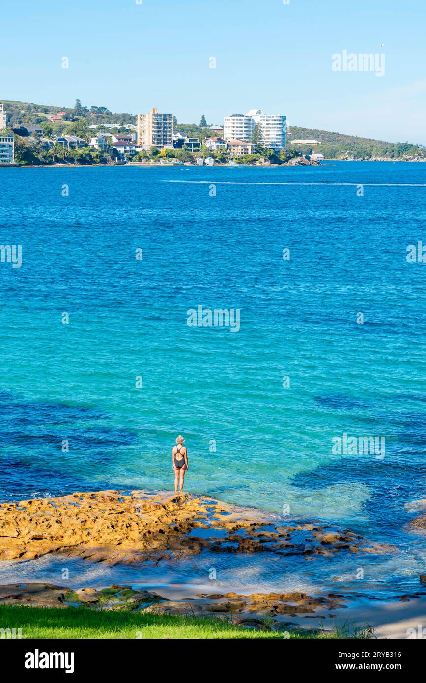 Una donna si prepara a tuffarsi in un cristallino porto di Sydney a Delwood (porto interno) Beach in una soleggiata mattinata d'inverno in Australia Foto Stock