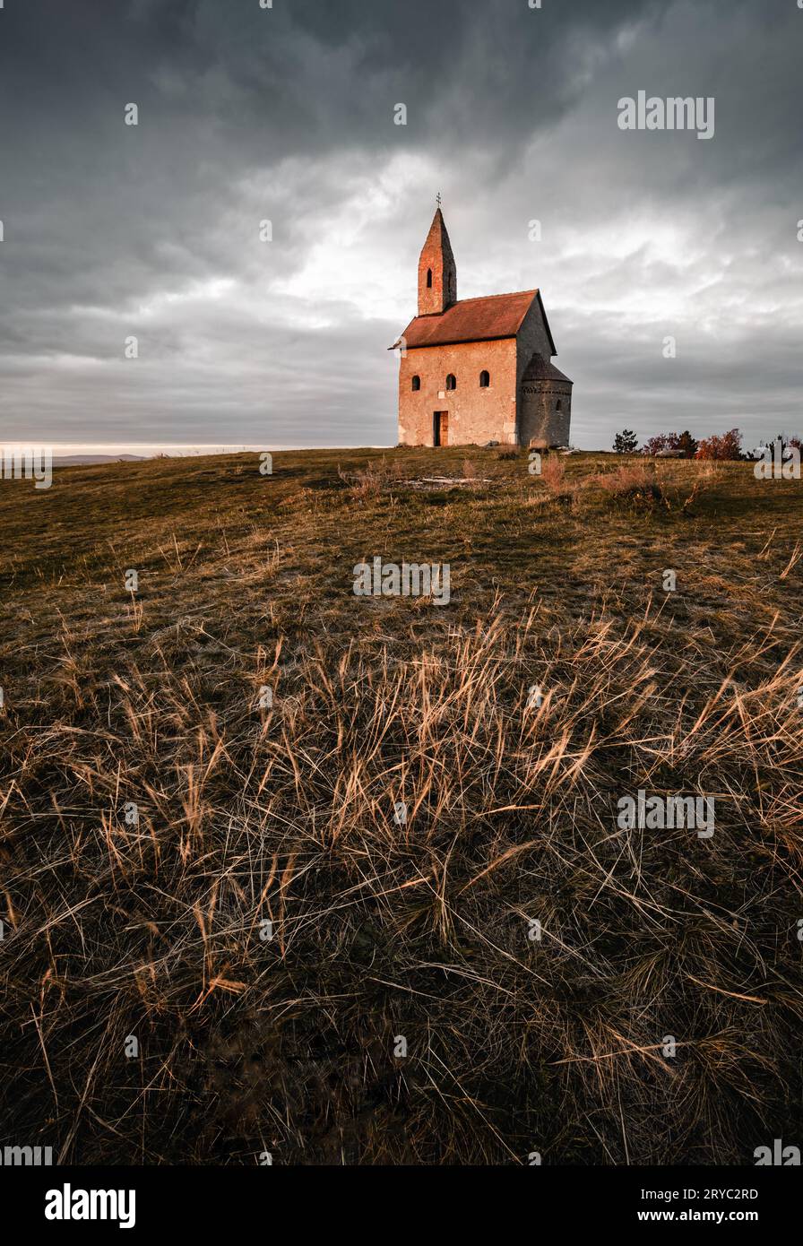 Foto verticale dell'antica chiesa cattolica di San Michael the Archangelwith cielo nuvoloso al tramonto - Drazovce, Slovacchia. Foto Stock