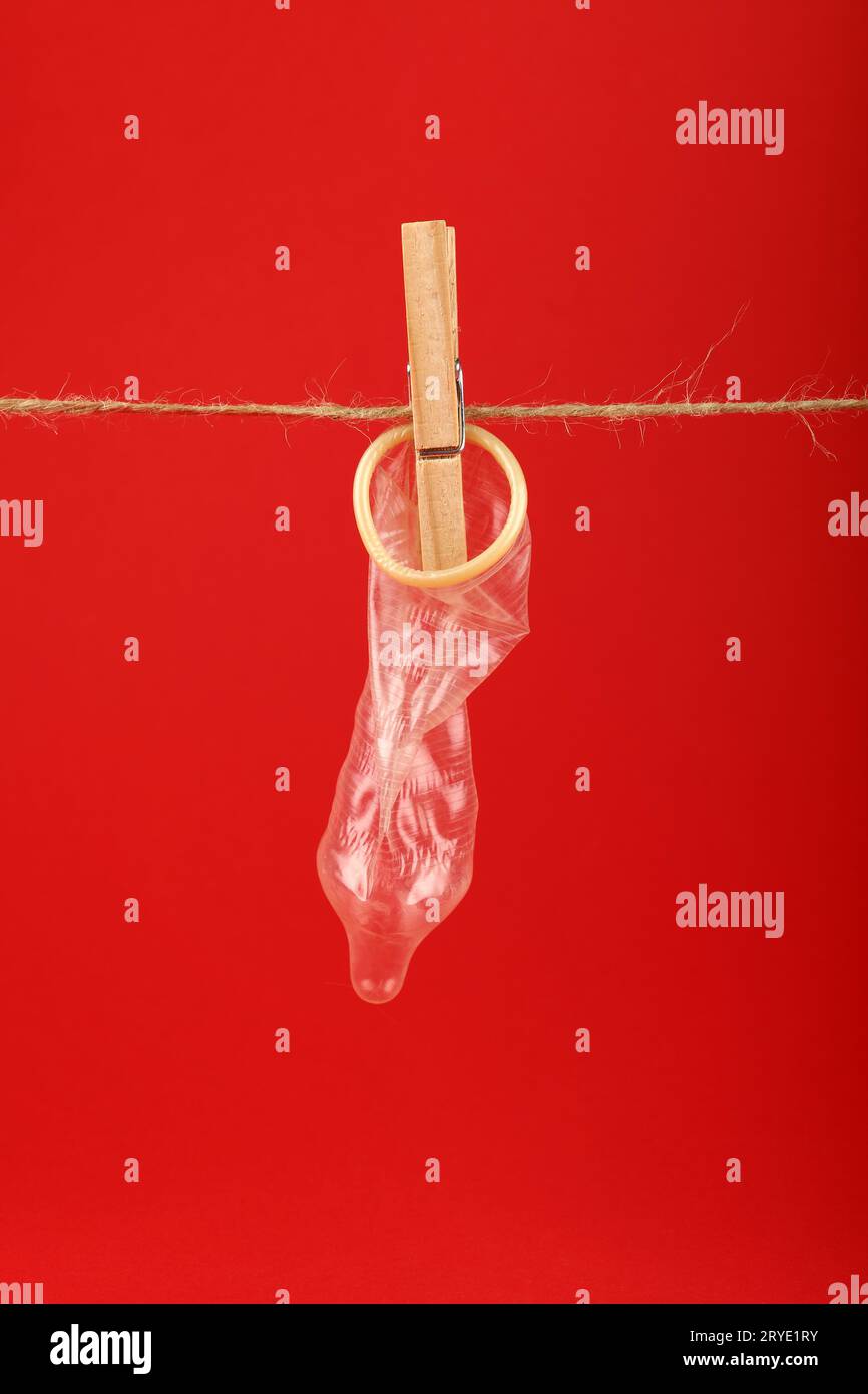 Un preservativo appeso sulla linea di lavaggio sopra il rosso Foto Stock