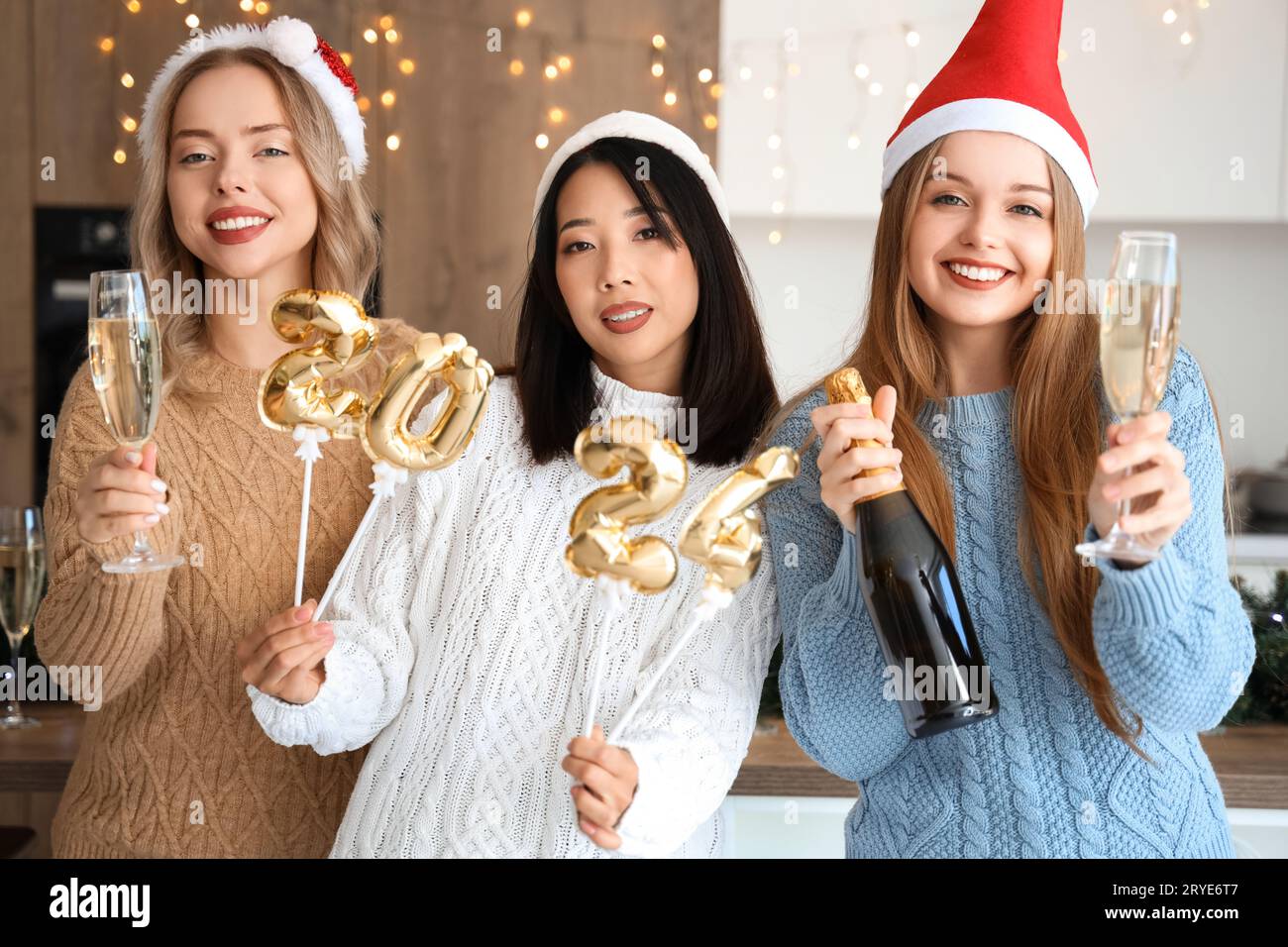 Giovani donne con champagne e figura 2024 che festeggiano il Natale in cucina Foto Stock