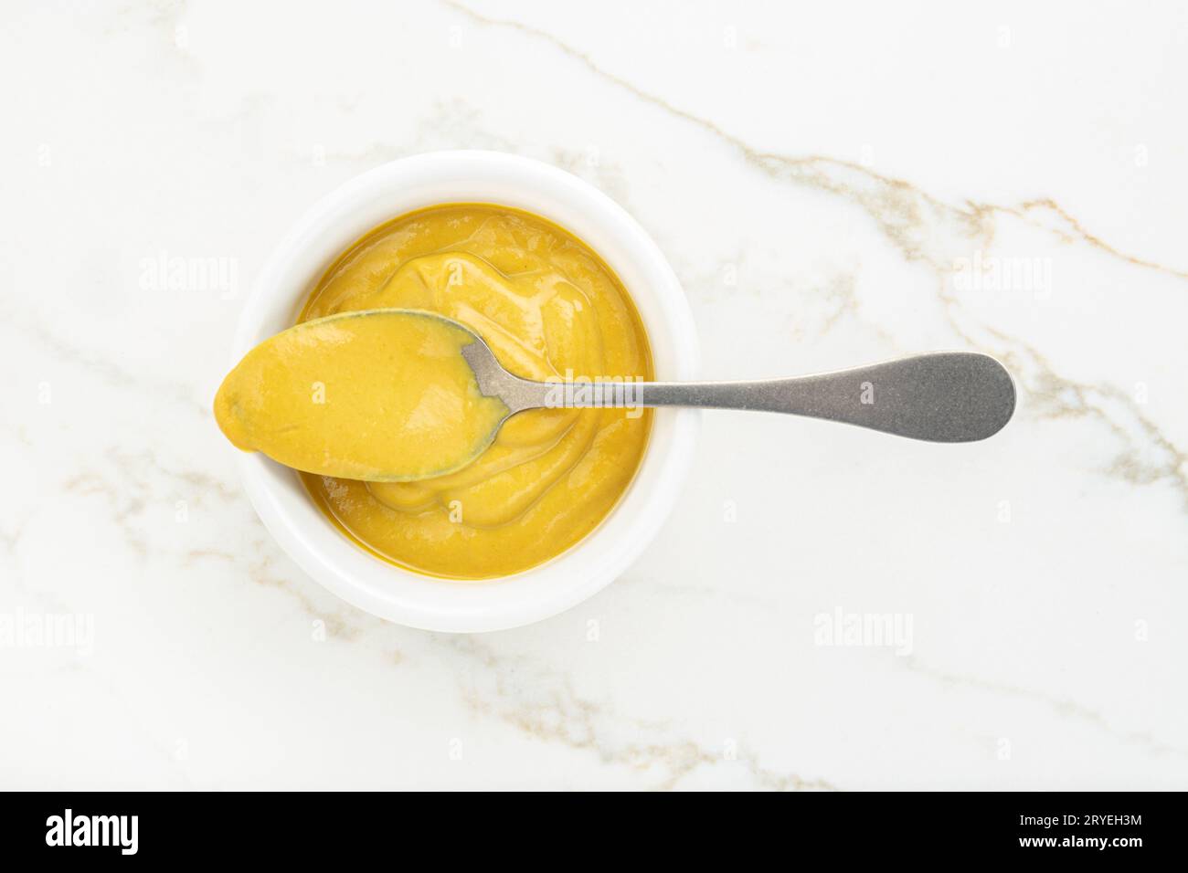 Salsa di senape in una ciotola e cucchiaio su un tavolo di marmo bianco Foto Stock