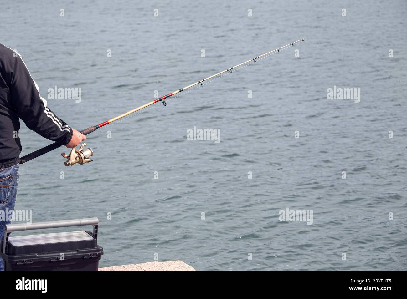 Pescatore in piedi sul bordo del molo con canna da pesca vicino al mare Foto Stock