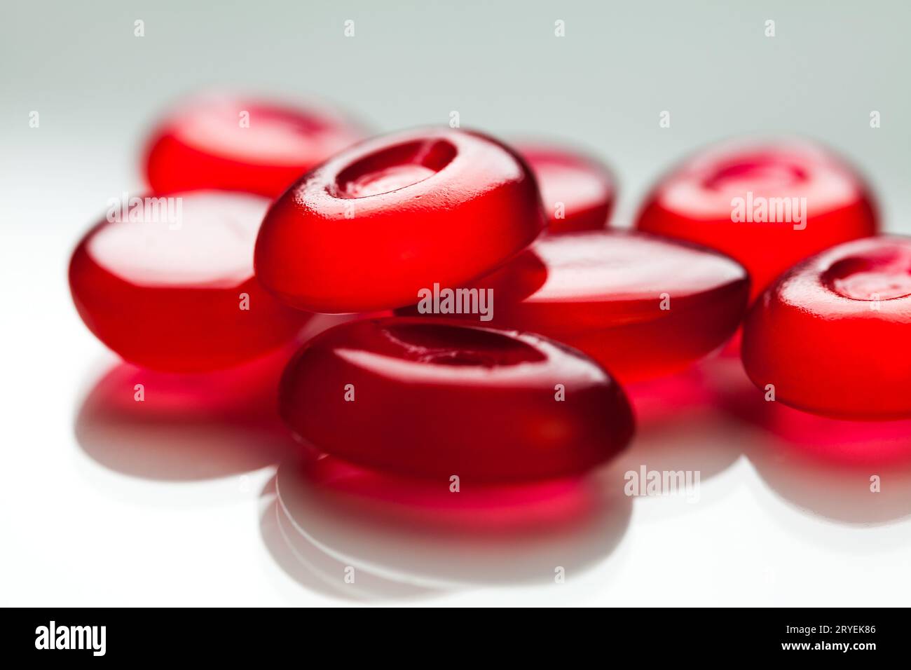 Pila di pillole rosse isolate su superficie bianca con riflesso Foto Stock