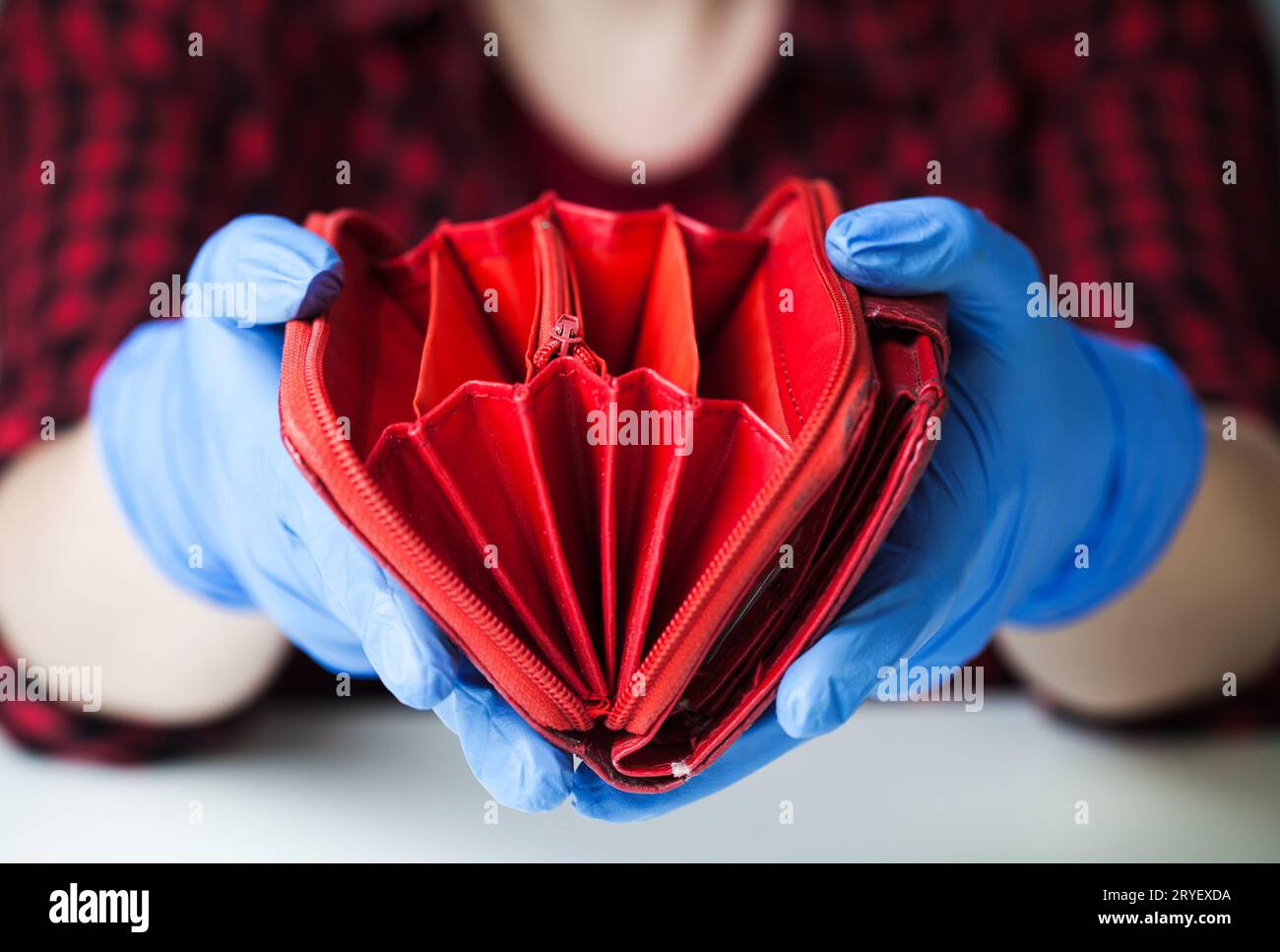 Persona che indossa guanti protettivi medici che tiene un portafoglio rosso vuoto Foto Stock