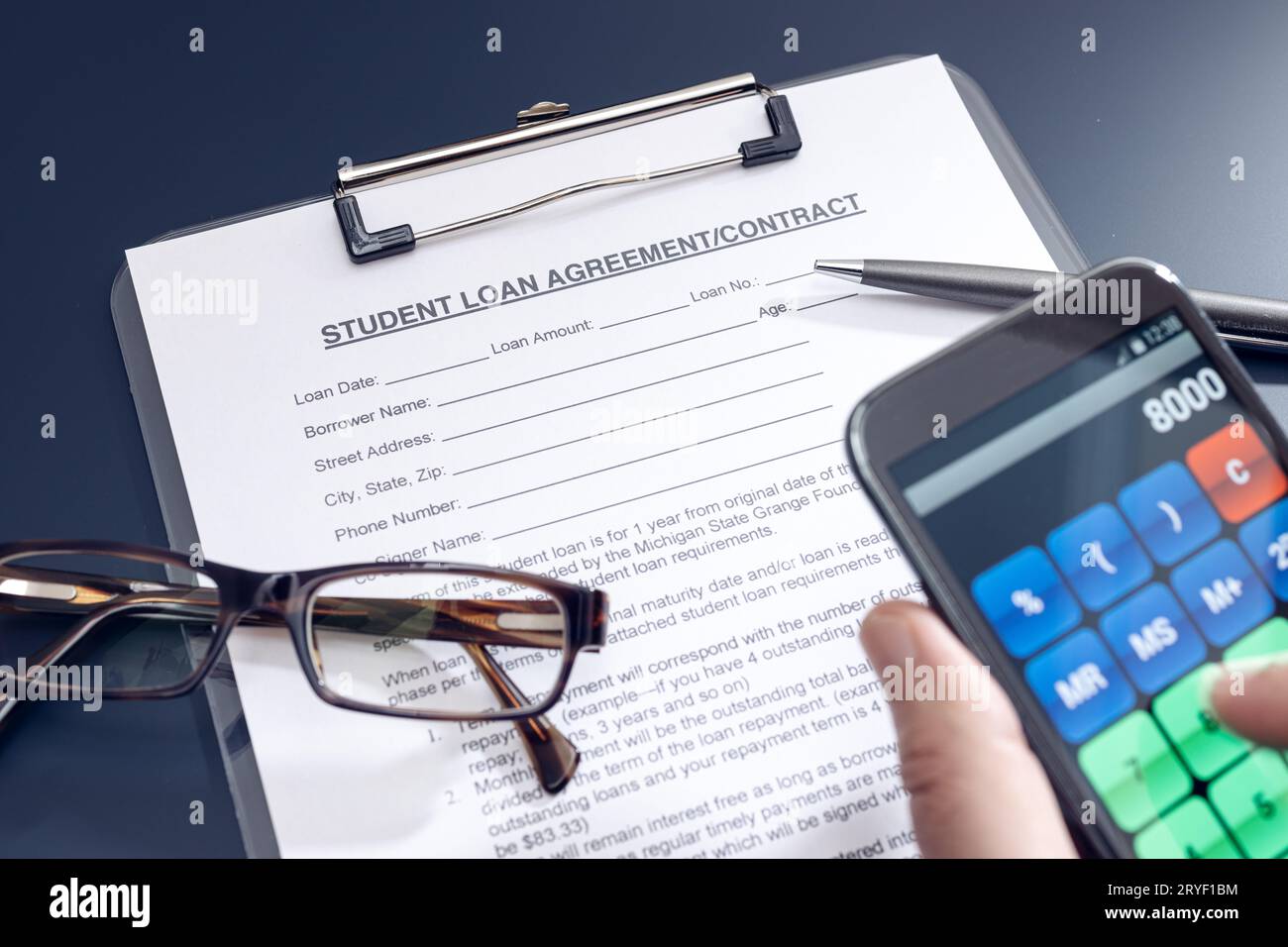 Richiesta di prestito per studenti vuota sul tavolo e mano con uno smartphone con l'app calcolatrice Foto Stock