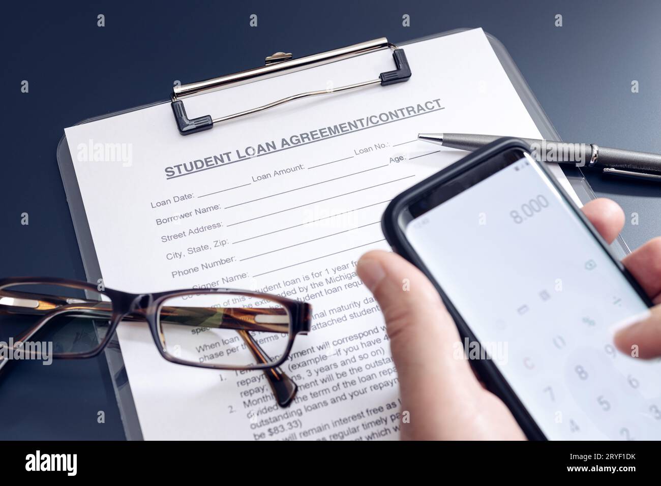 Richiesta di prestito per studenti vuota sul tavolo e mano con uno smartphone con l'app calcolatrice Foto Stock