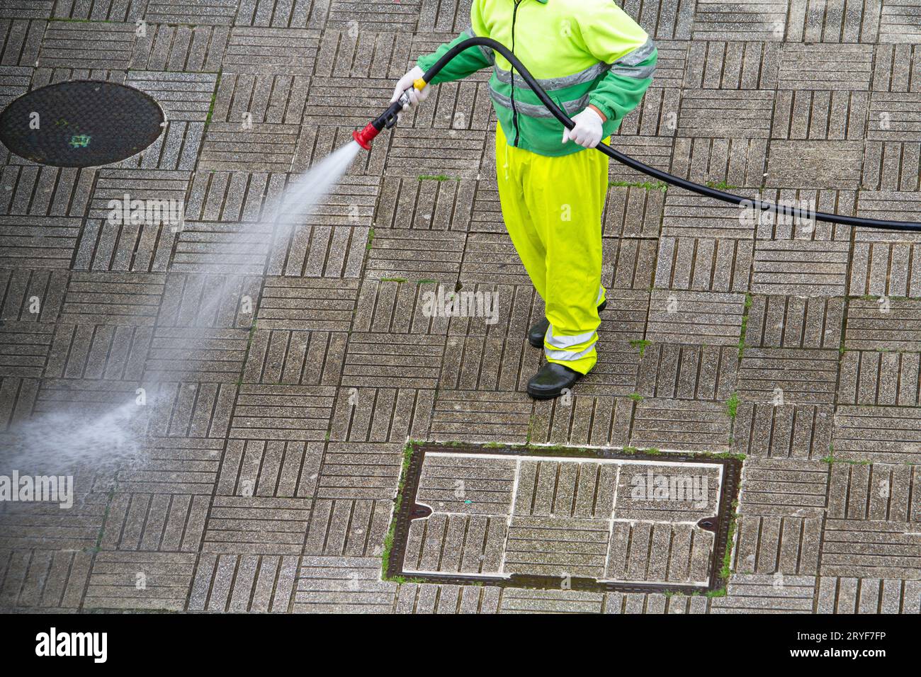 Lavoratore che tiene un tubo flessibile per pulire un marciapiede con acqua. Concetto di manutenzione urbana o pulizia Foto Stock