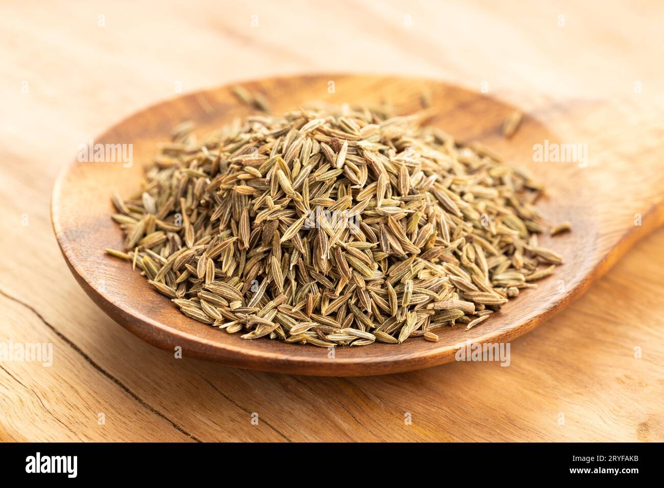 Semi di cumino su cucchiaio di legno su tavola. Cumino Cimino Foto Stock