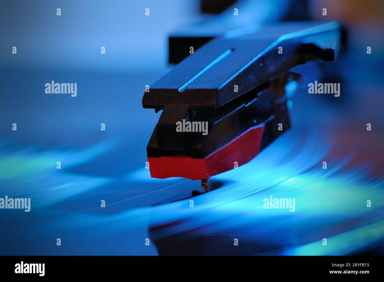 Foto ravvicinata di un guscio, una cartuccia e un ago di un lettore di dischi che riproduce un LP in vinile. La spia blu illumina la registrazione. Foto Stock