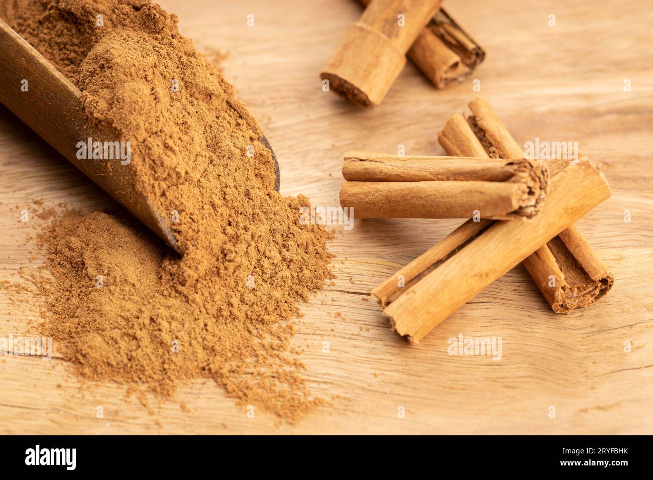 Polvere di cannella e bastoncini di cannella in paletta di legno su tavola di legno. Primo piano Foto Stock