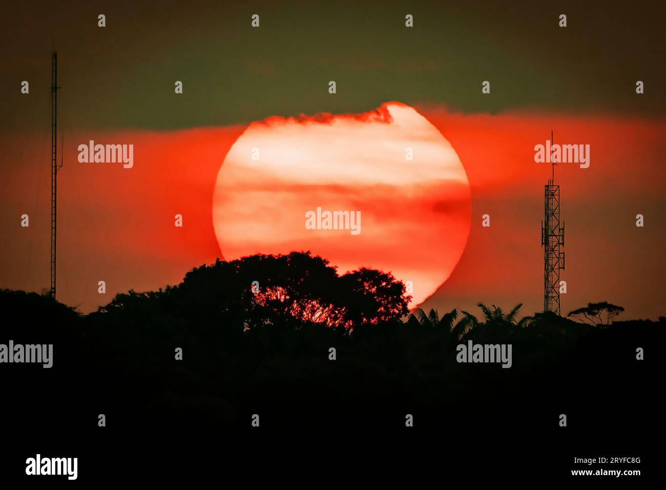 Grande sole al tramonto, silhouette urbana con antenne e alberi Foto Stock