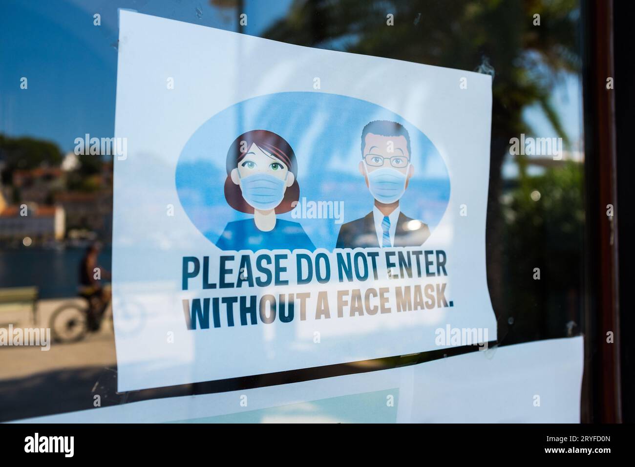 SI PREGA DI NON ENTRARE SENZA Un cartello con LA MASCHERA FACCIALE sulla porta di vetro del negozio o dell'ufficio Foto Stock