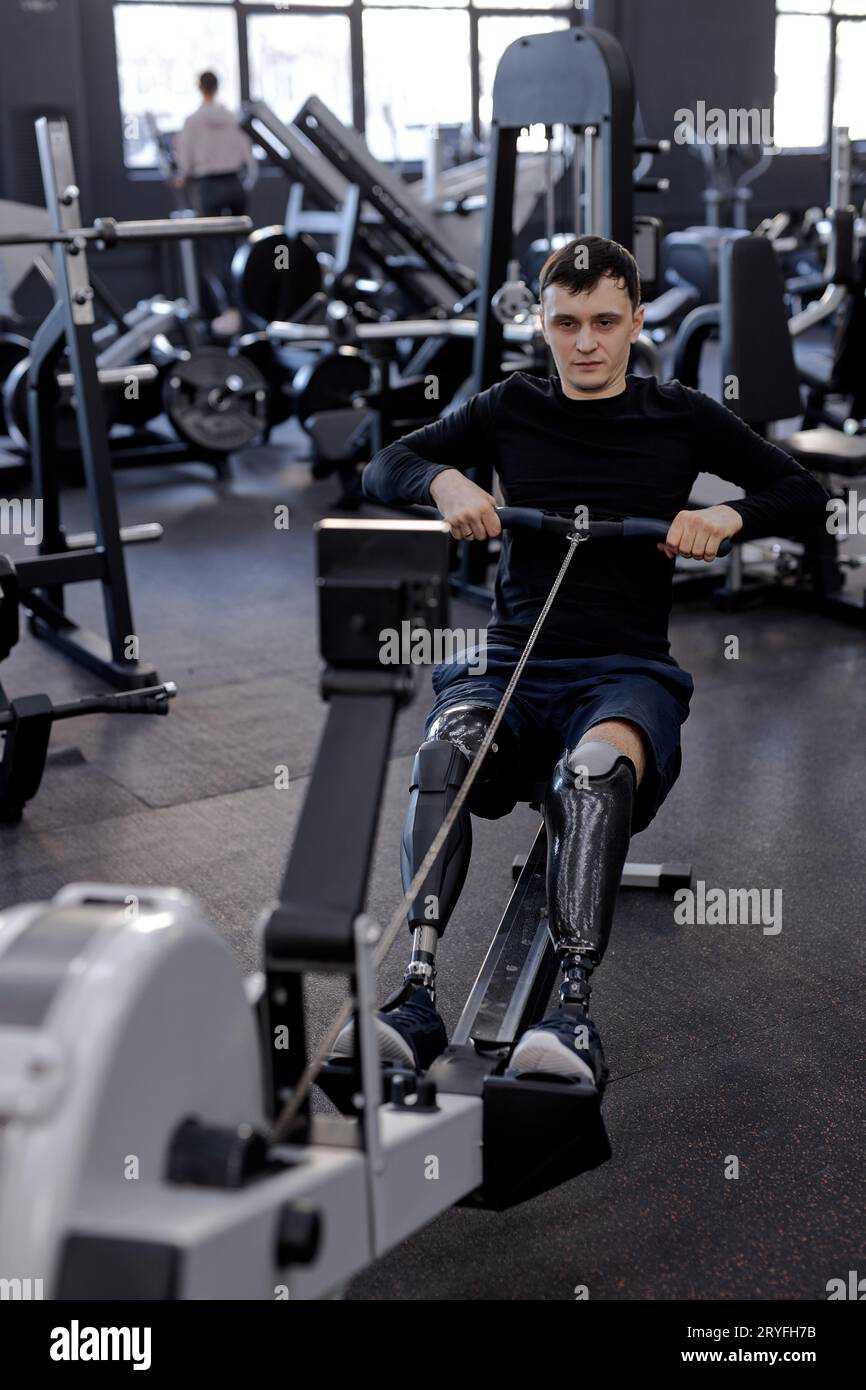 uomo stanco e sudato che si allena con la macchina da canottaggio in palestra, tiro completo. motivazione, resistenza, forza di volontà Foto Stock