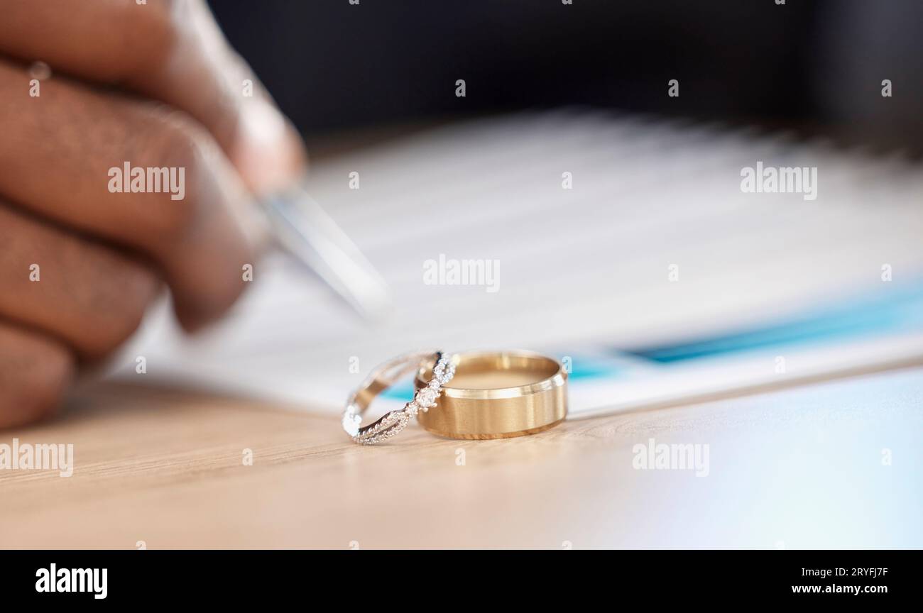 Divorzio, anelli e firma su documenti per un avvocato, registrazione di nozze o scrittura di un contratto. Tabella, primo piano e certificato, pianificazione o legale Foto Stock