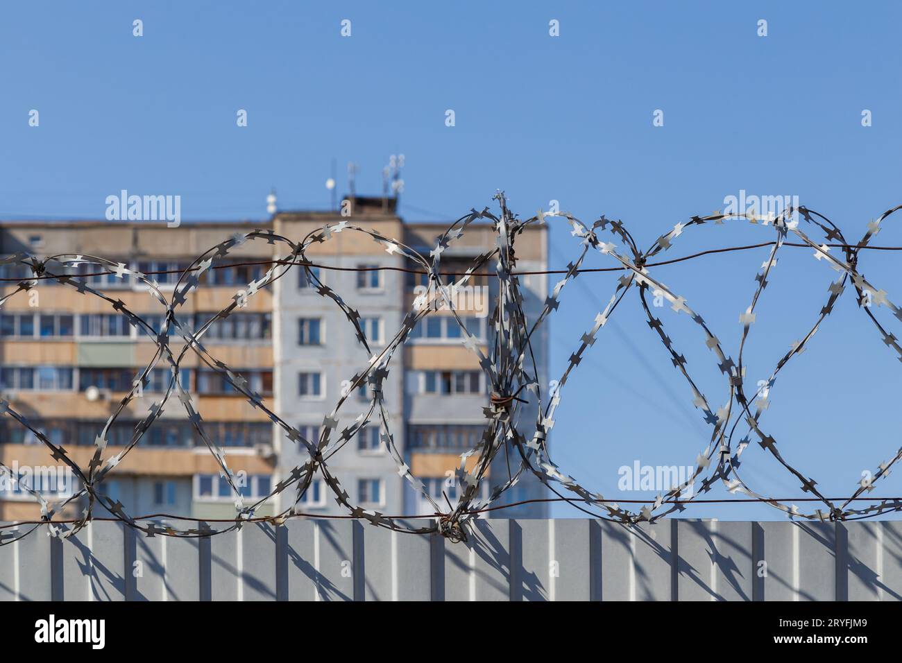 Edificio residenziale a piu' piani dietro una recinzione con filo spinato alla luce del giorno, il concetto di prigione, restrizione di liberati Foto Stock