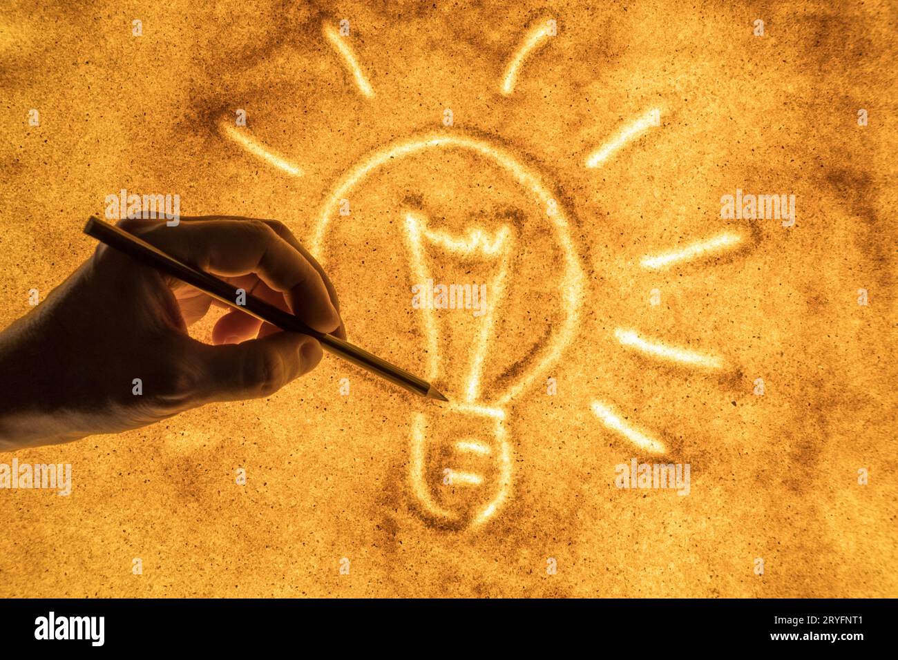 Mano che disegna una lampadina sulla sabbia illuminata. Concetto di una nuova idea. Foto Stock