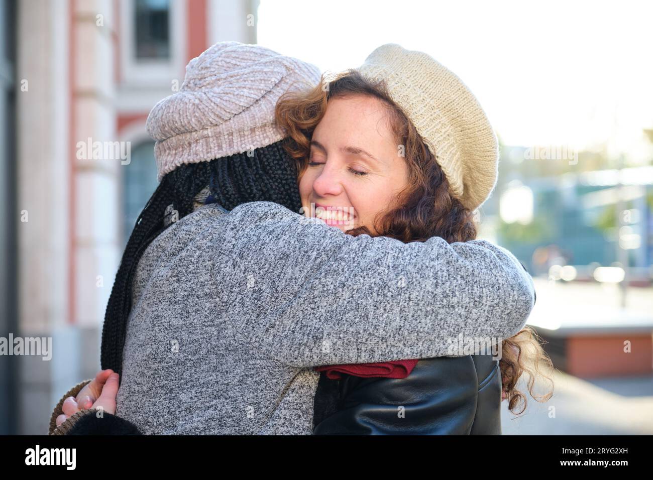 Due donne multirazziali felici amici abbracciarsi e sorridere sulla strada della città. Foto Stock