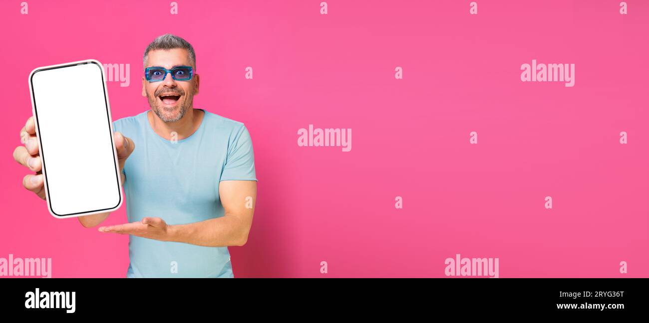 Smartphone in mano a un uomo affascinante, Guy 30s 40 in camicia blu casual e occhiali da sole isolati su sfondo rosa. Uomo con telefono Foto Stock