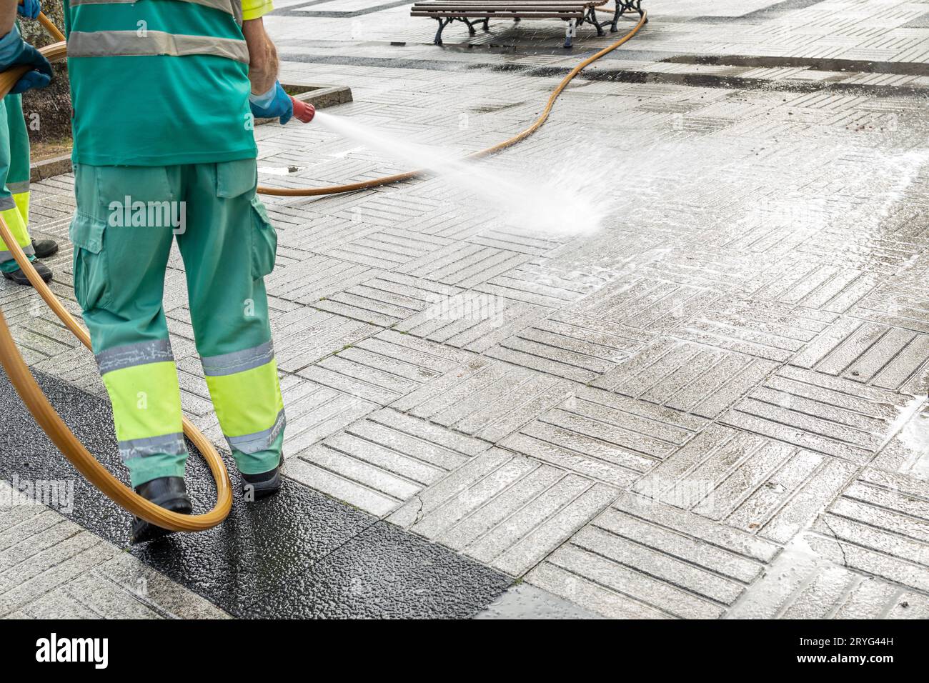 Operaio che pulisce una piazza della città con acqua usando un tubo flessibile. Concetto di manutenzione pubblica. Spazio di copia Foto Stock