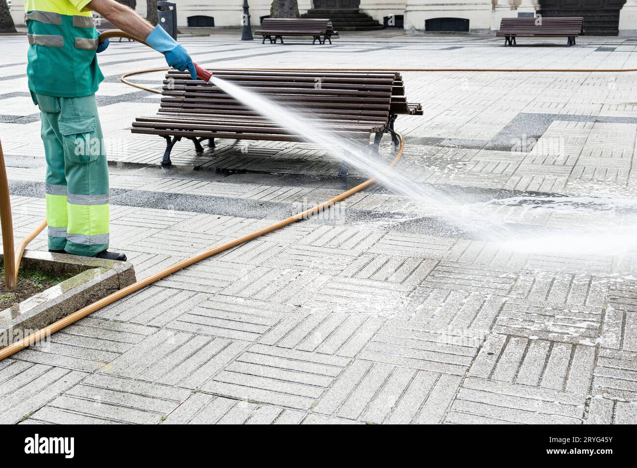 Lavoratore che pulisce una piazza della città con acqua usando una cannula. Concetto di manutenzione del parco pubblico. Copia spazio Foto Stock