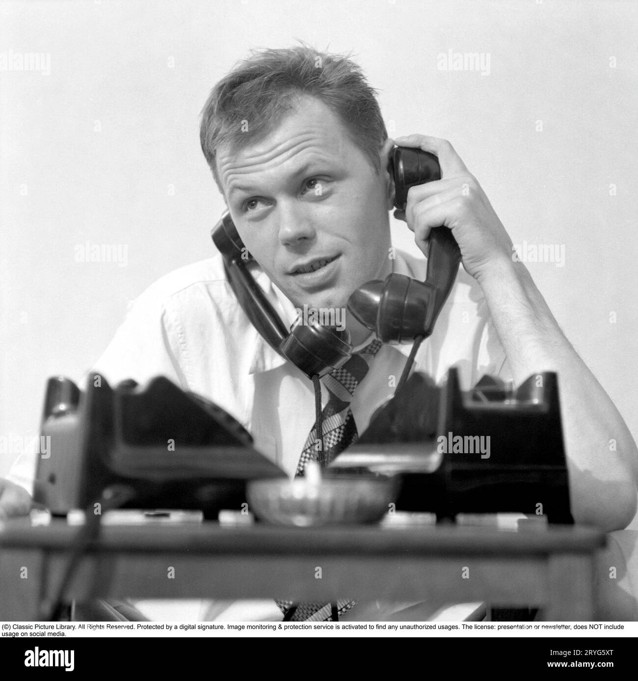Negli anni '1950 Sixten Larsson con due telefoni che sembrano occupati e sembra che stia parlando in due ricevitori contemporaneamente, uno contro ogni orecchio. Svezia 1952. Rif. Conard 2020 Foto Stock