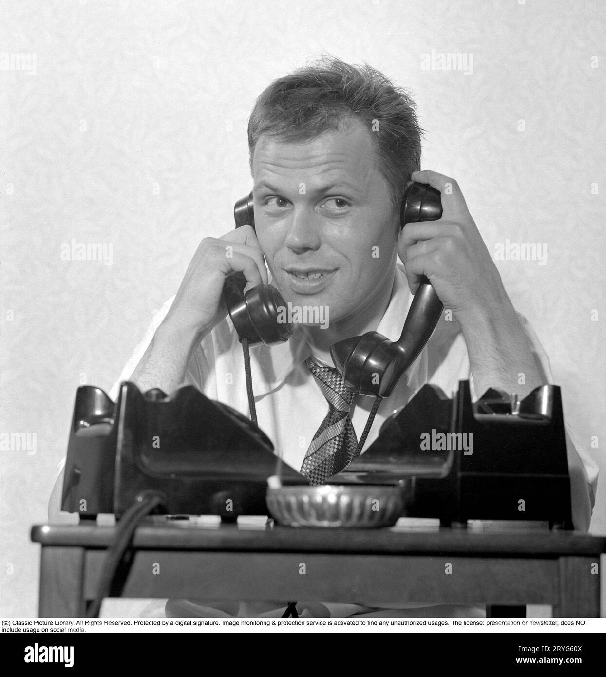 Negli anni '1950 Sixten Larsson con due telefoni che sembrano occupati e sembra che stia parlando in due ricevitori contemporaneamente, uno contro ogni orecchio. Svezia 1952. Rif. Conard 2020 Foto Stock