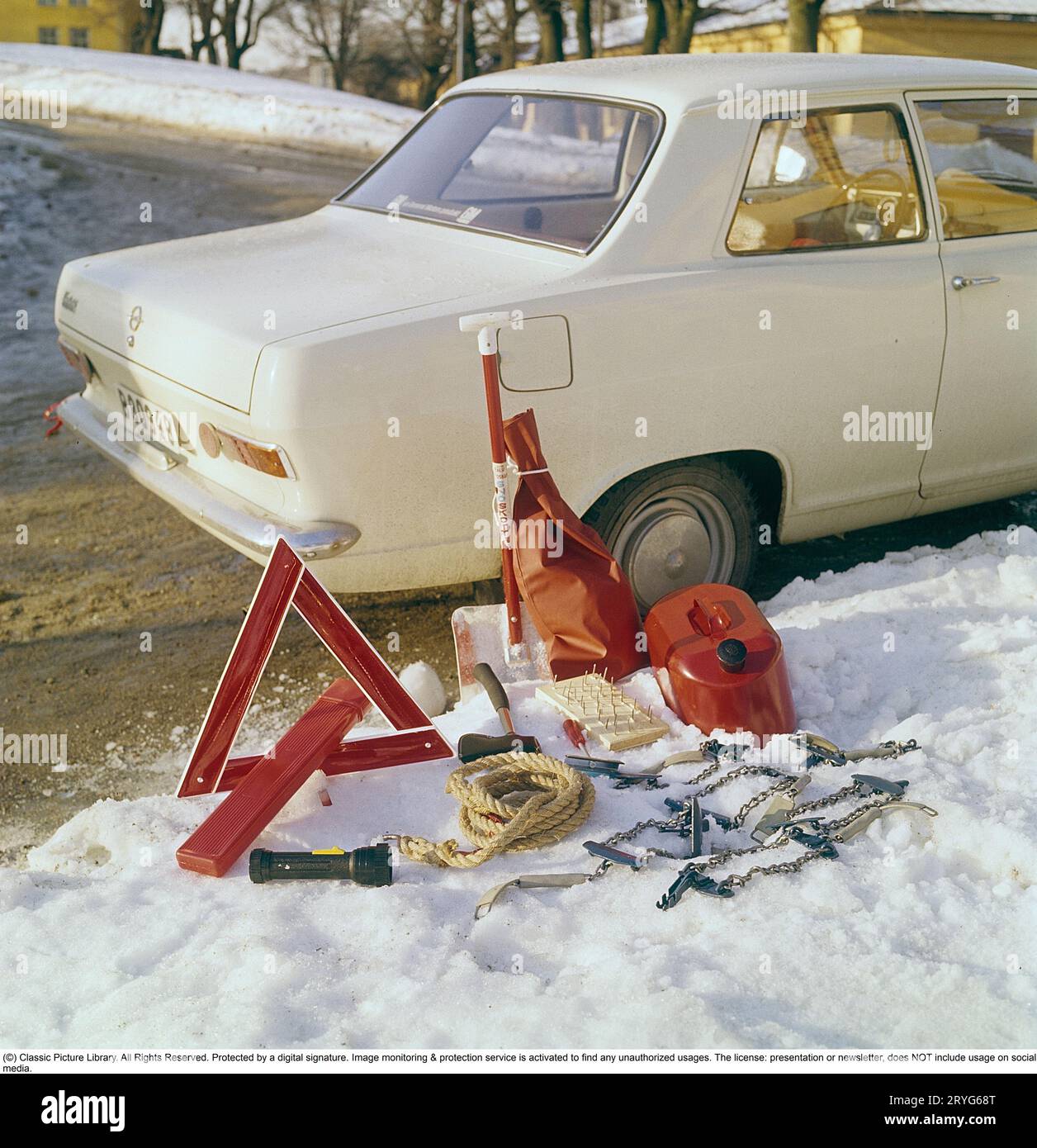 Accessori per auto negli anni '1960 Un Opel bianco funge da sfondo per questa immagine che mostra gli accessori adatti alla guida invernale. Oltre all'ovvio triangolo segnaletico, è presente anche una pala da neve, un cavo di traino, un'ascia, una tanica di carburante di riserva e catene da neve. Con tutto questo nel bagagliaio, non rimane molto spazio per nient'altro. Svezia 1969 Foto Stock