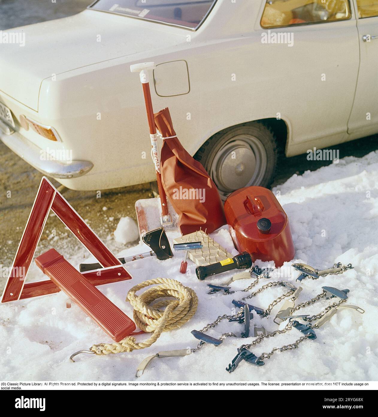 Accessori per auto negli anni '1960 Un Opel bianco funge da sfondo per questa immagine che mostra gli accessori adatti alla guida invernale. Oltre all'ovvio triangolo segnaletico, è presente anche una pala da neve, un cavo di traino, un'ascia, una tanica di carburante di riserva e catene da neve. Con tutto questo nel bagagliaio, non rimane molto spazio per nient'altro. Svezia 1969 Foto Stock
