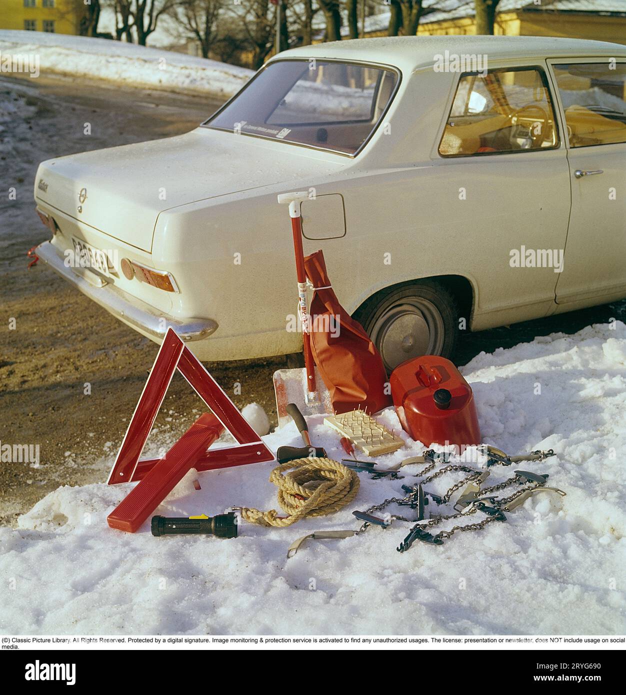 Accessori per auto negli anni '1960 Un Opel bianco funge da sfondo per questa immagine che mostra gli accessori adatti alla guida invernale. Oltre all'ovvio triangolo segnaletico, è presente anche una pala da neve, un cavo di traino, un'ascia, una tanica di carburante di riserva e catene da neve. Con tutto questo nel bagagliaio, non rimane molto spazio per nient'altro. Svezia 1969 Foto Stock