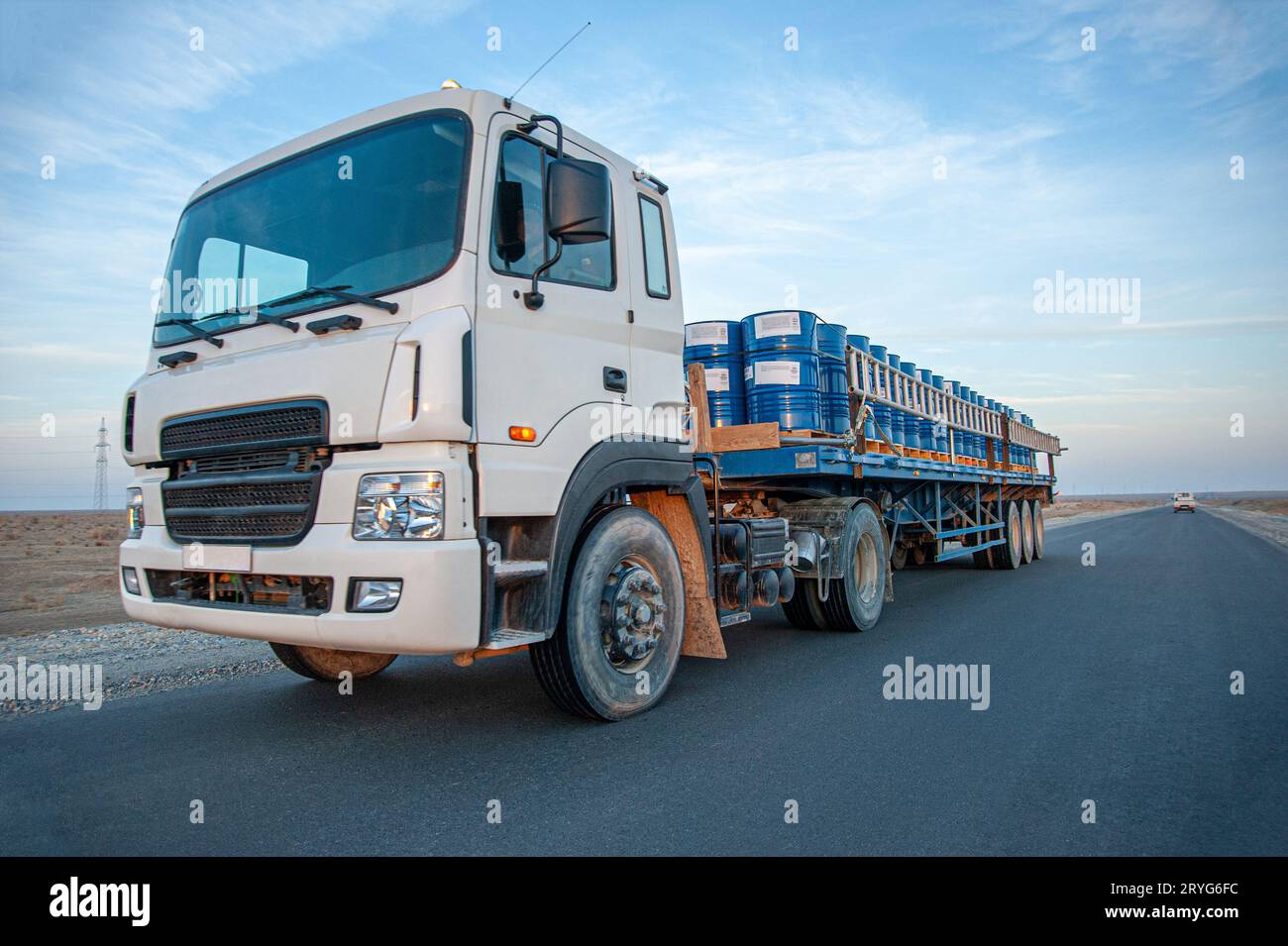 Un camion con barili di metallo sulla strada contro un bel cielo Foto Stock