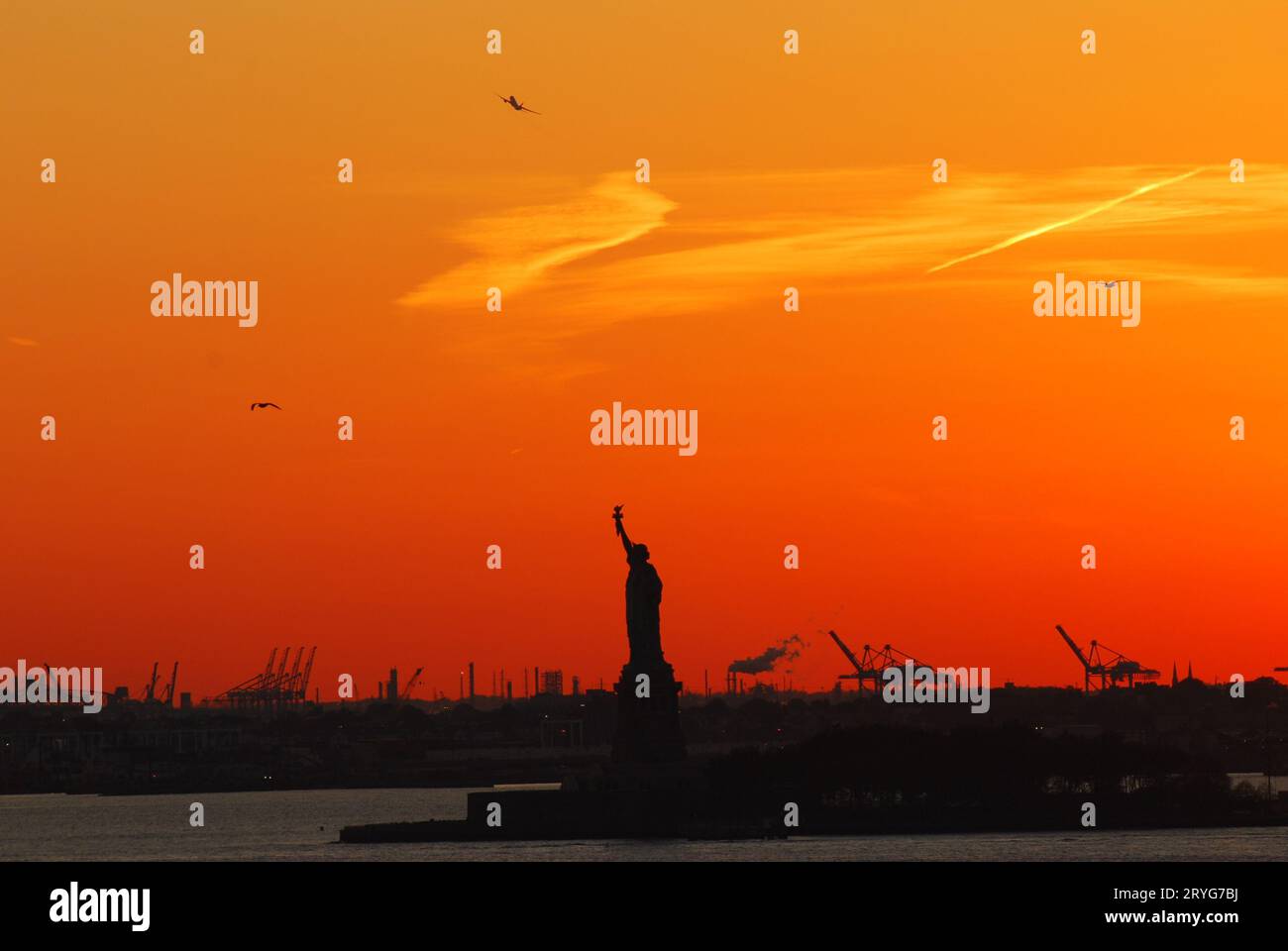 Silhouette della Statua della libertà e Liberty Island a New York contro un cielo arancione tramonto Foto Stock