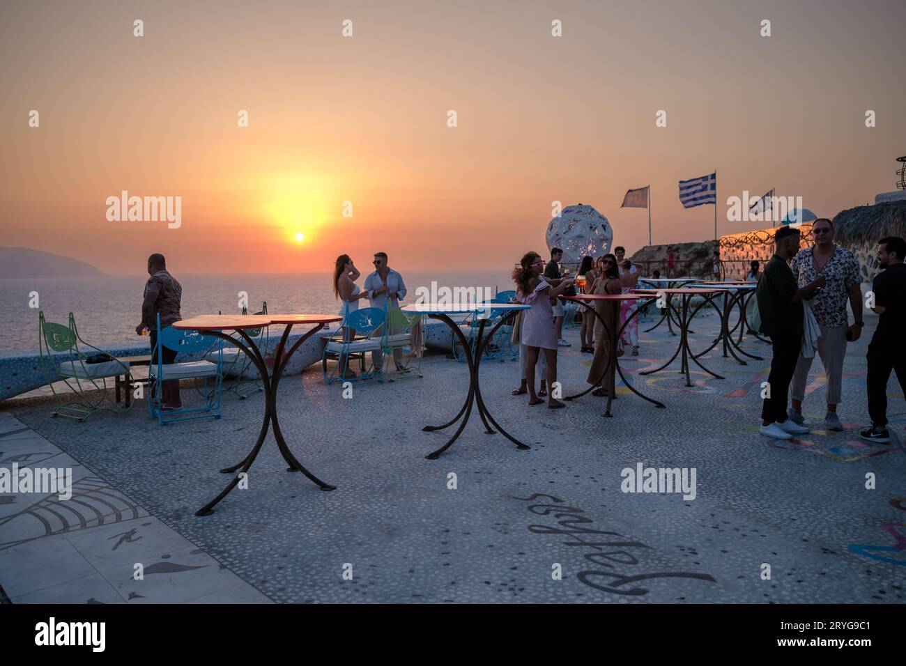 IOS, Grecia - 8 settembre 2023: I turisti si godono un drink e una vista mozzafiato sul Mar Egeo con un tramonto arancione in un lounge bar in Grecia Foto Stock