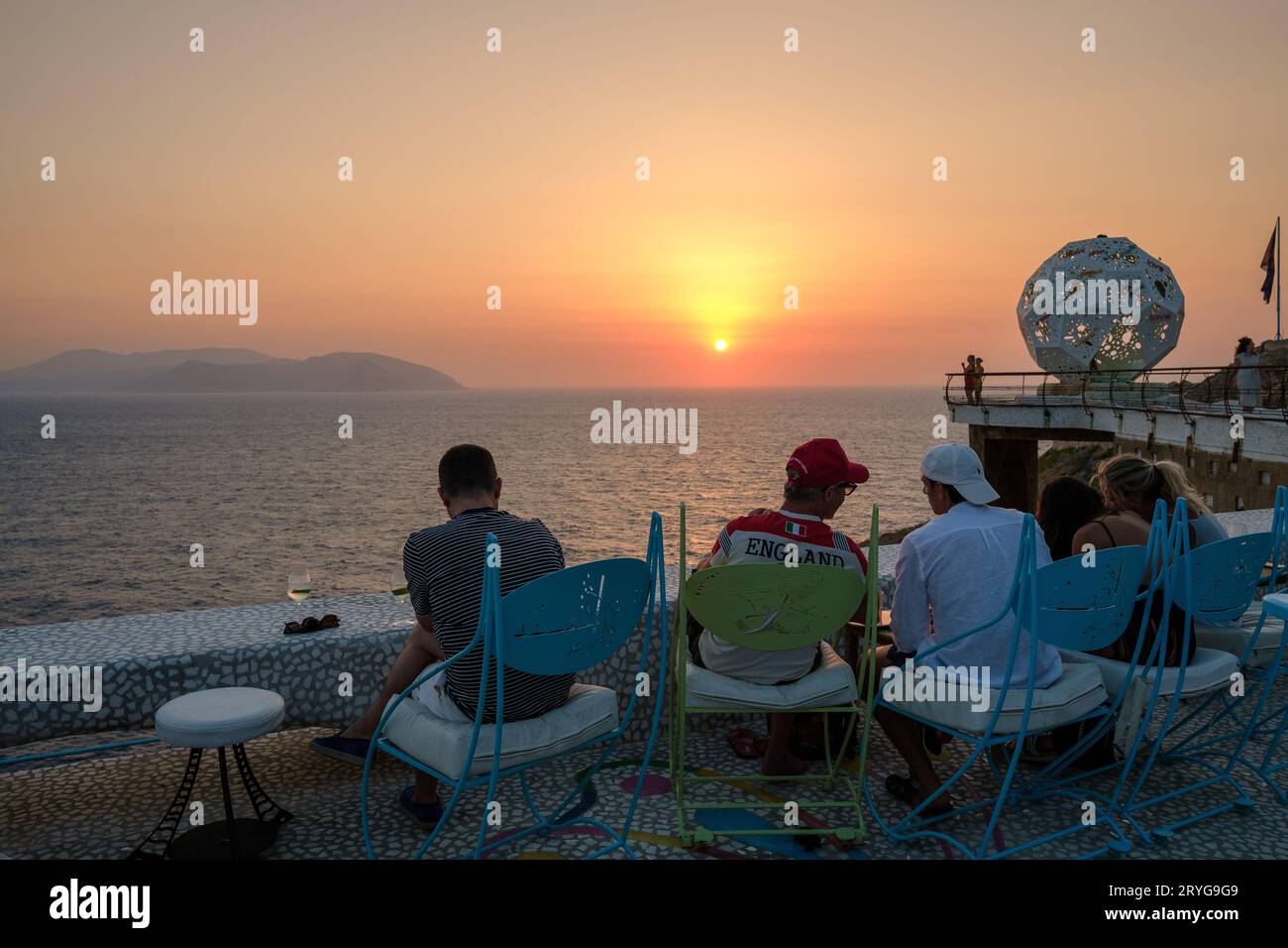 IOS, Grecia - 8 settembre 2023: I turisti si godono un drink e una vista mozzafiato sul Mar Egeo con un tramonto arancione in un lounge bar in Grecia Foto Stock
