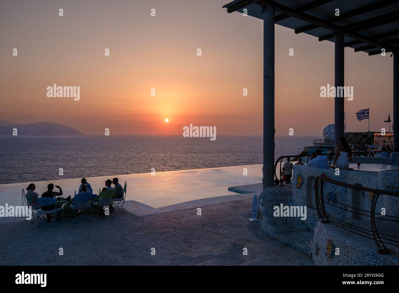 IOS, Grecia - 8 settembre 2023: I turisti si godono un drink e una vista mozzafiato sul Mar Egeo con un tramonto arancione in un lounge bar in Grecia Foto Stock