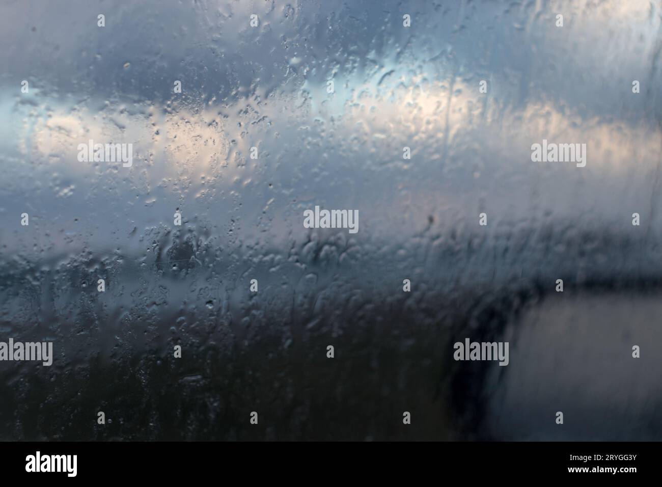 La pioggia fa cadere l'acqua sul finestrino dell'auto. vista dalla superficie dell'auto con finestrino in vetro e gocce d'acqua in una giornata di pioggia Foto Stock