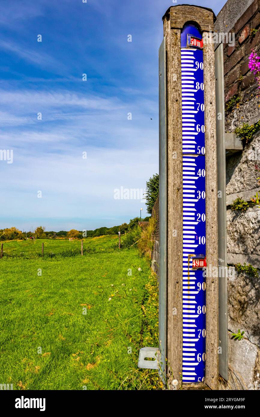 Scala idrometrica accanto a un muro sulla pianura alluvionale accanto al fiume Maas, misura l'altezza delle acque del fiume, soleggiate e nebbiose giornate estive con cielo blu Foto Stock