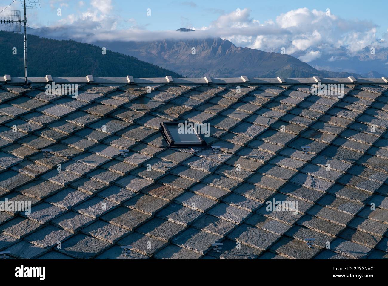 tetto con piastrelle di pietra, tipico delle case di montagna, pietre di granito grigio blu, montagne sullo sfondo. isolamento termico, classe energetica. Foto Stock