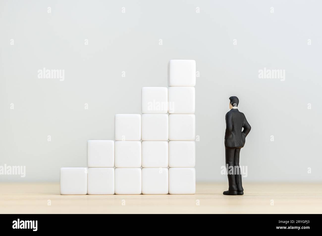 Figurina uomo d'affari che guarda un gruppo di blocchi che formano una scala ascendente. Copia spazio Foto Stock