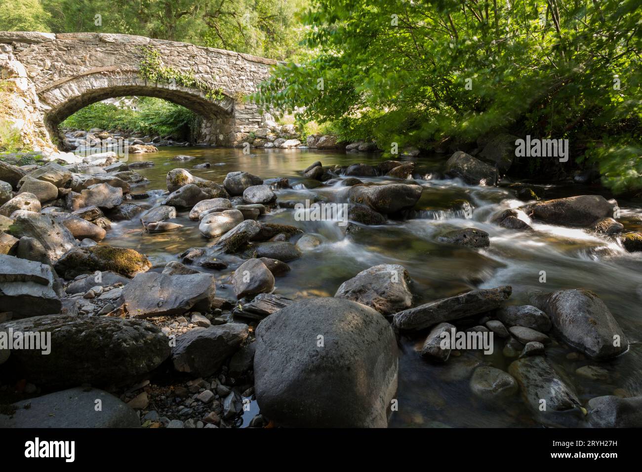 Ponte di pietra su un fiume con massi. Abergwynant, Gwynedd, Galles. Giugno. Foto Stock