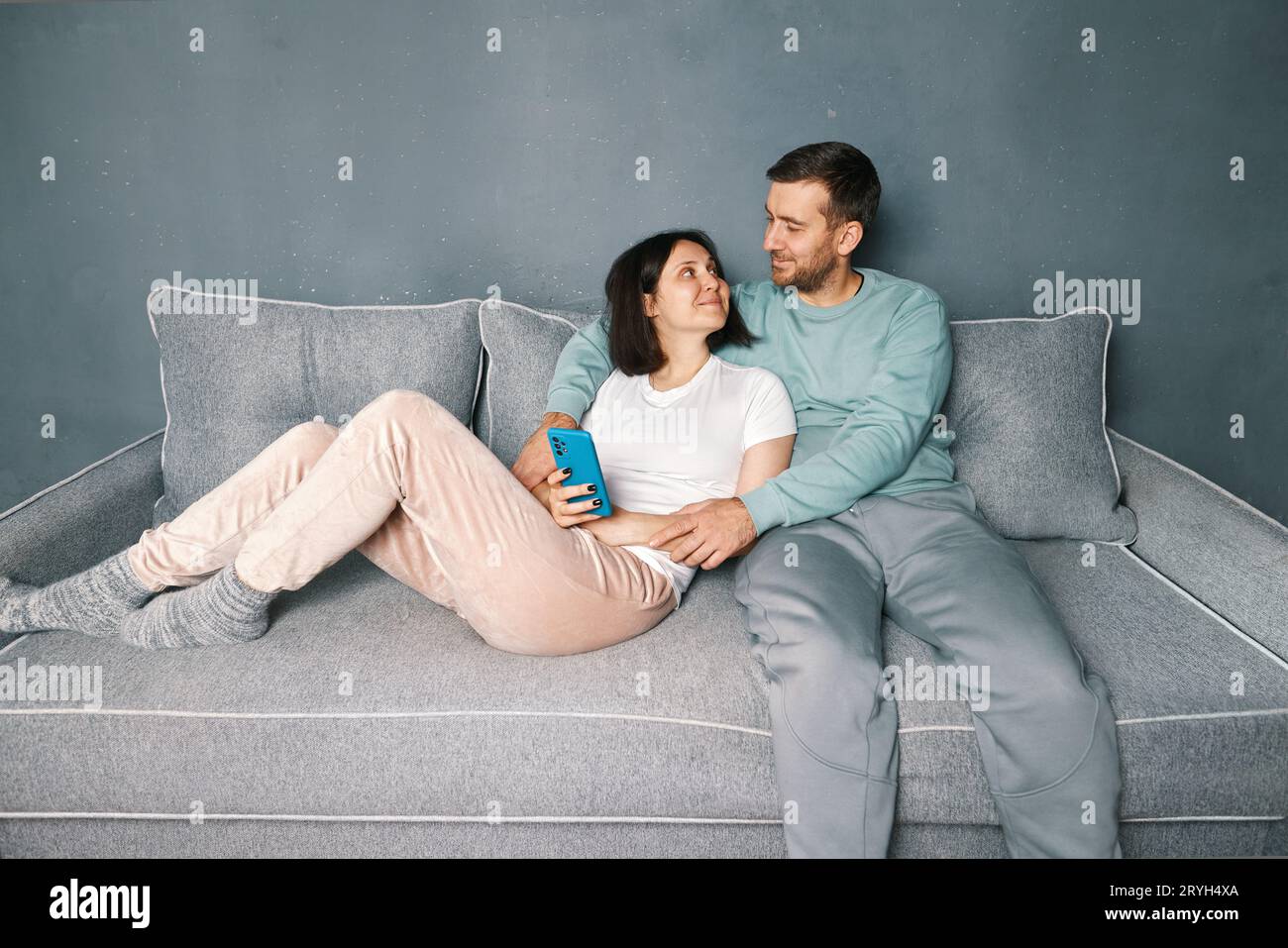 Un uomo sorridente che abbraccia sua moglie e si rilassa sul divano Foto Stock