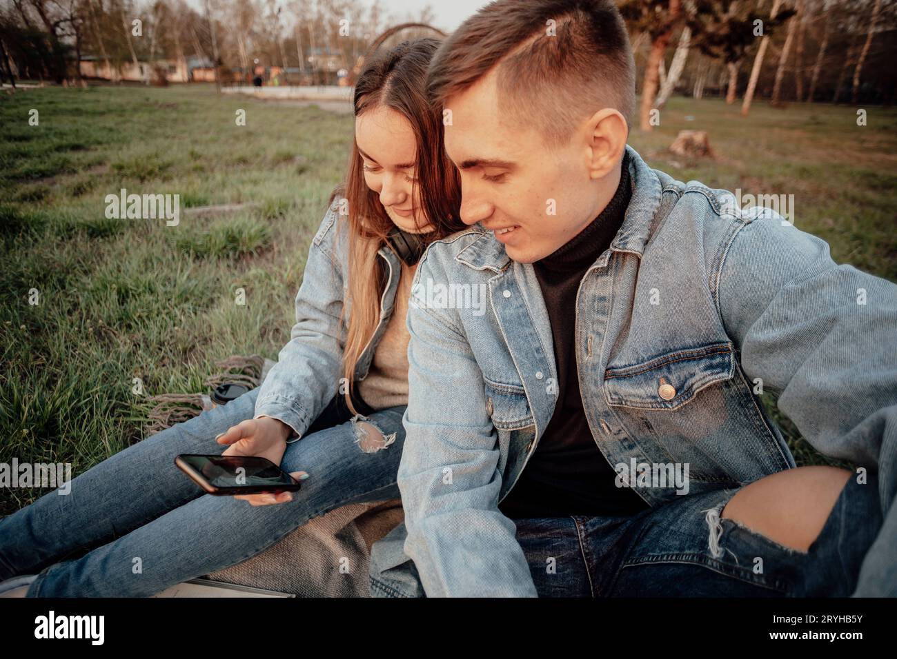 Una giovane coppia di studenti alla moda sorride mentre guardano il telefono nel parco Foto Stock