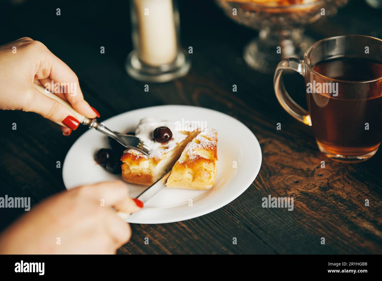 Immagine ravvicinata di una donna che mangia pasticcini alla ciliegia con forchetta e coltello nel caffè Foto Stock