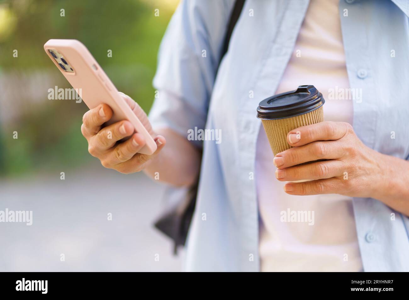 La foto ravvicinata si concentra sulle mani di una donna che tiene un telefono cellulare e una tazza di carta da caffè. L'immagine raffigura lo stile di vita moderno e. Foto Stock