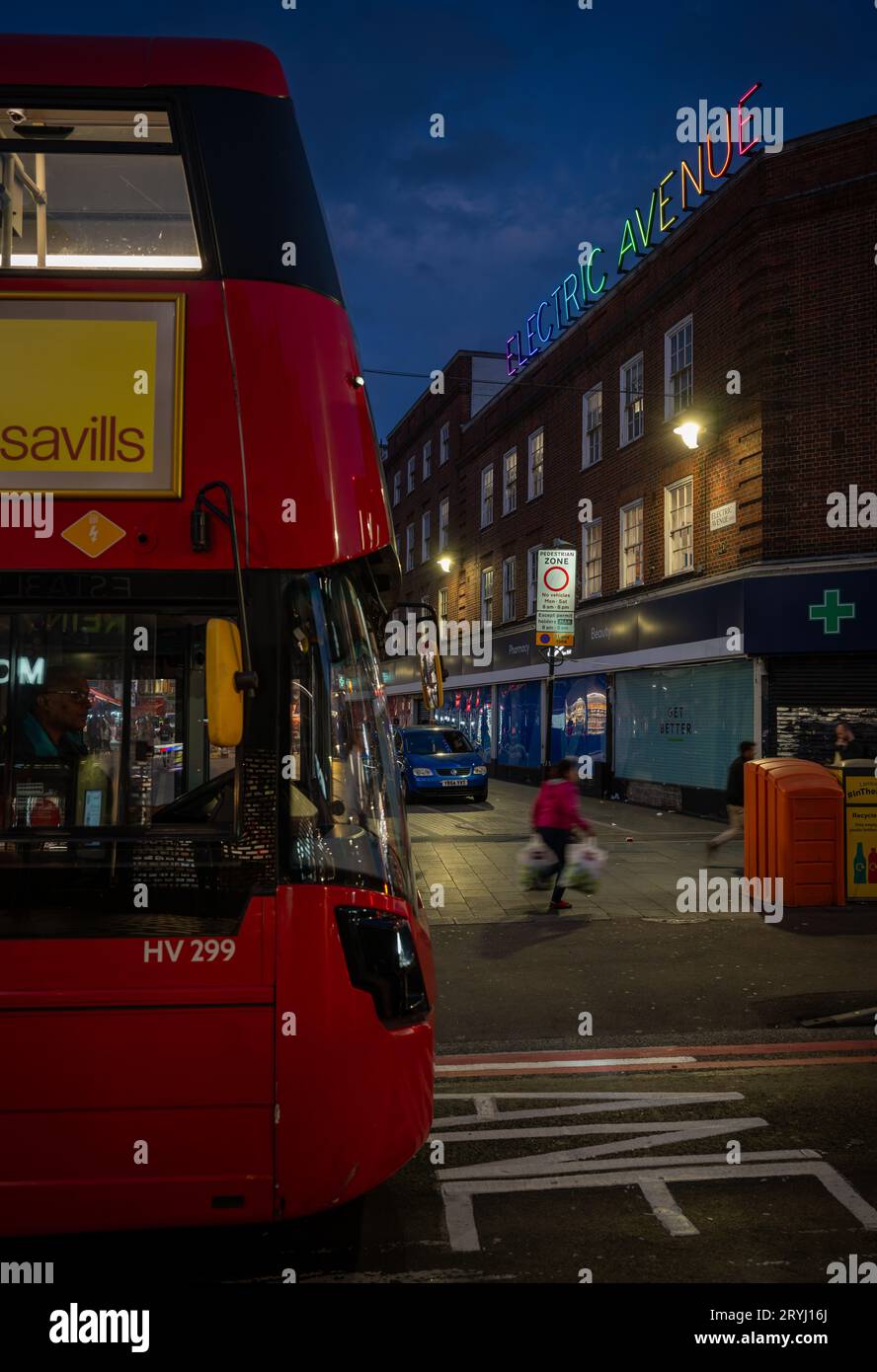 Brixton, Londra, Regno Unito: Un autobus rosso di Londra che viaggia lungo Brixton Road di notte. All'incrocio con Electric Avenue e la sua colorata insegna al neon. Foto Stock