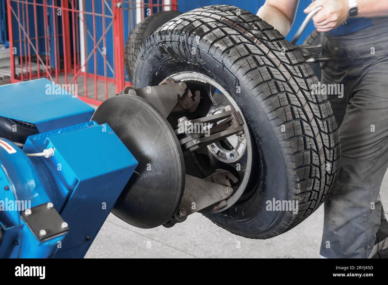 Meccanico lavora in un'officina di riparazione pneumatici. Il meccanico addetto all'assistenza auto posiziona la ruota sul cerchione dell'auto utilizzando un dispositivo speciale. Sostituzione degli pneumatici invernali in officina. Foto Stock