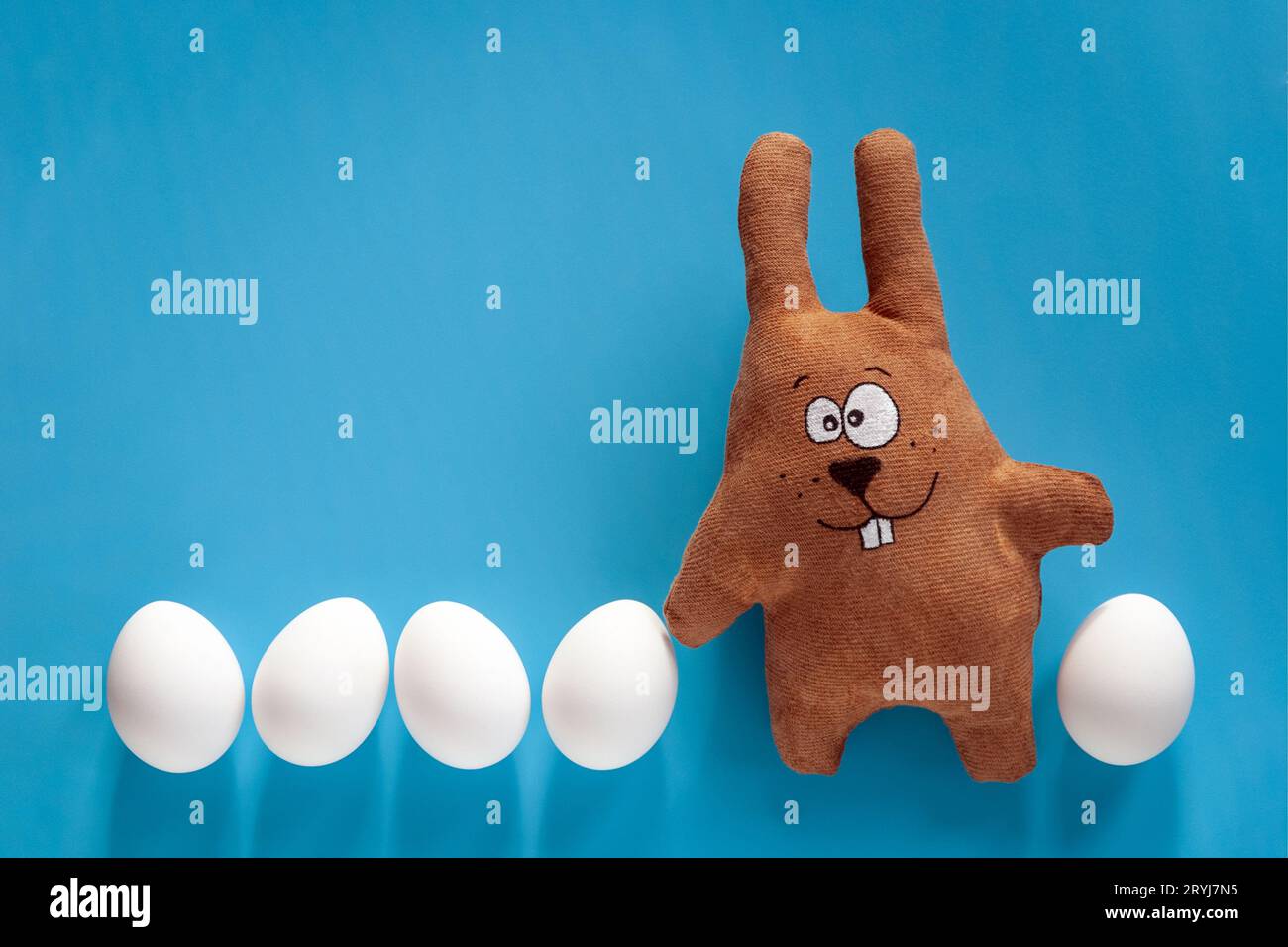 Caccia di Pasqua con coniglietto giocattolo e uova colorate in vetro su sfondo blu Foto Stock