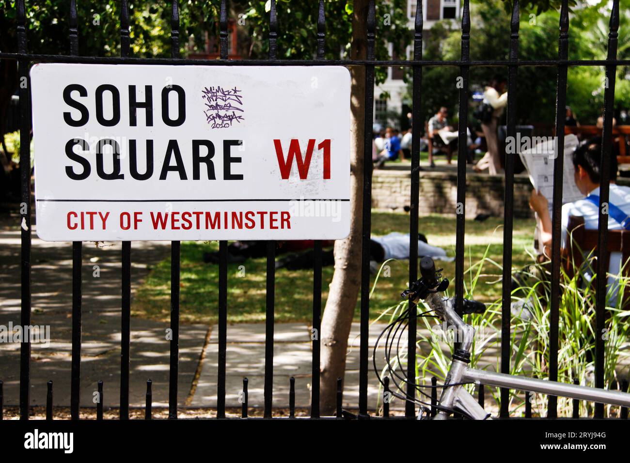 Soho Square W1 cartello bianco di Westminster con parco sullo sfondo e persona che legge il giornale al sole Foto Stock