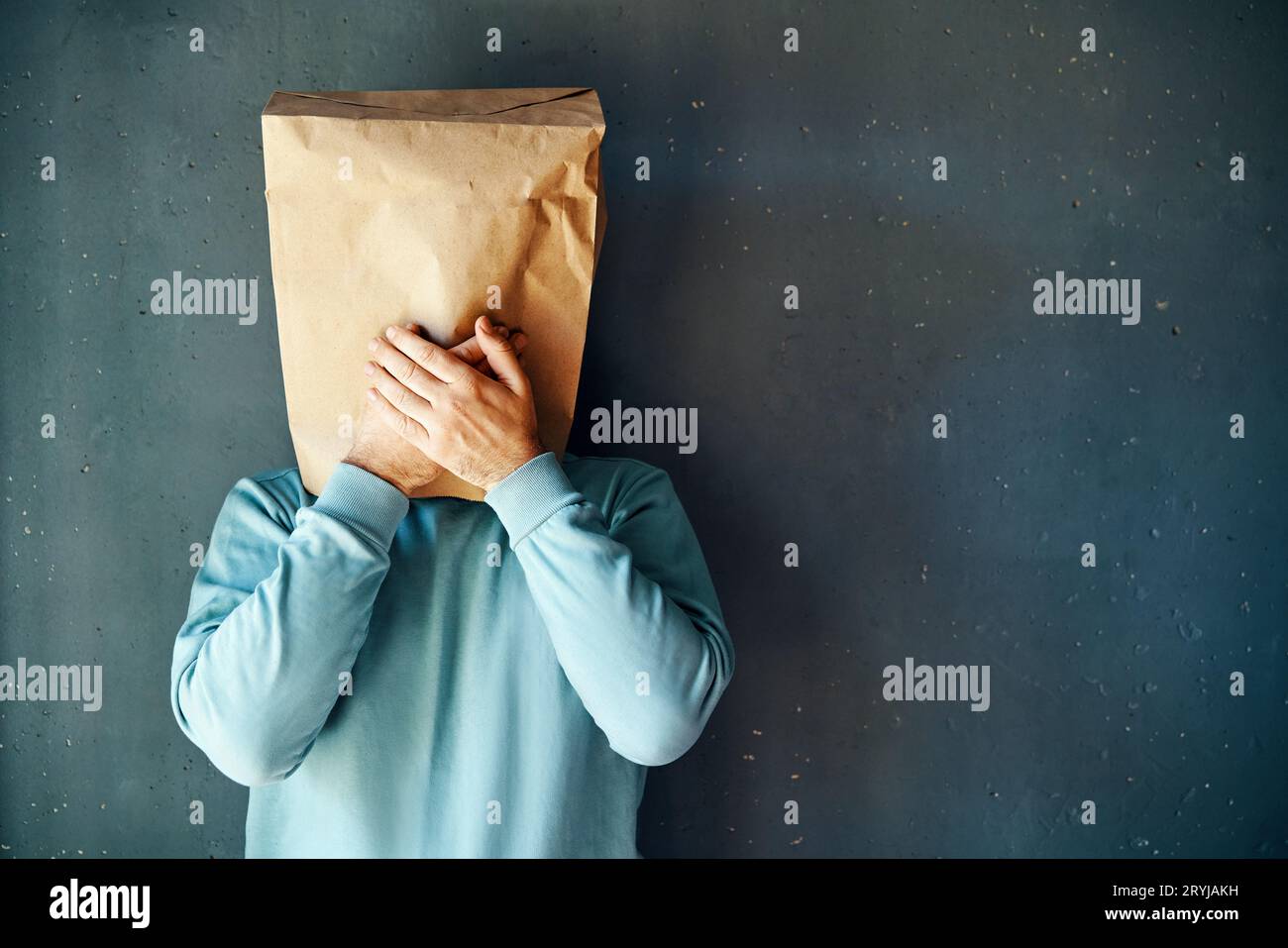 Uomo con un sacchetto di carta sulla testa che copre la bocca con le mani su sfondo grigio Foto Stock